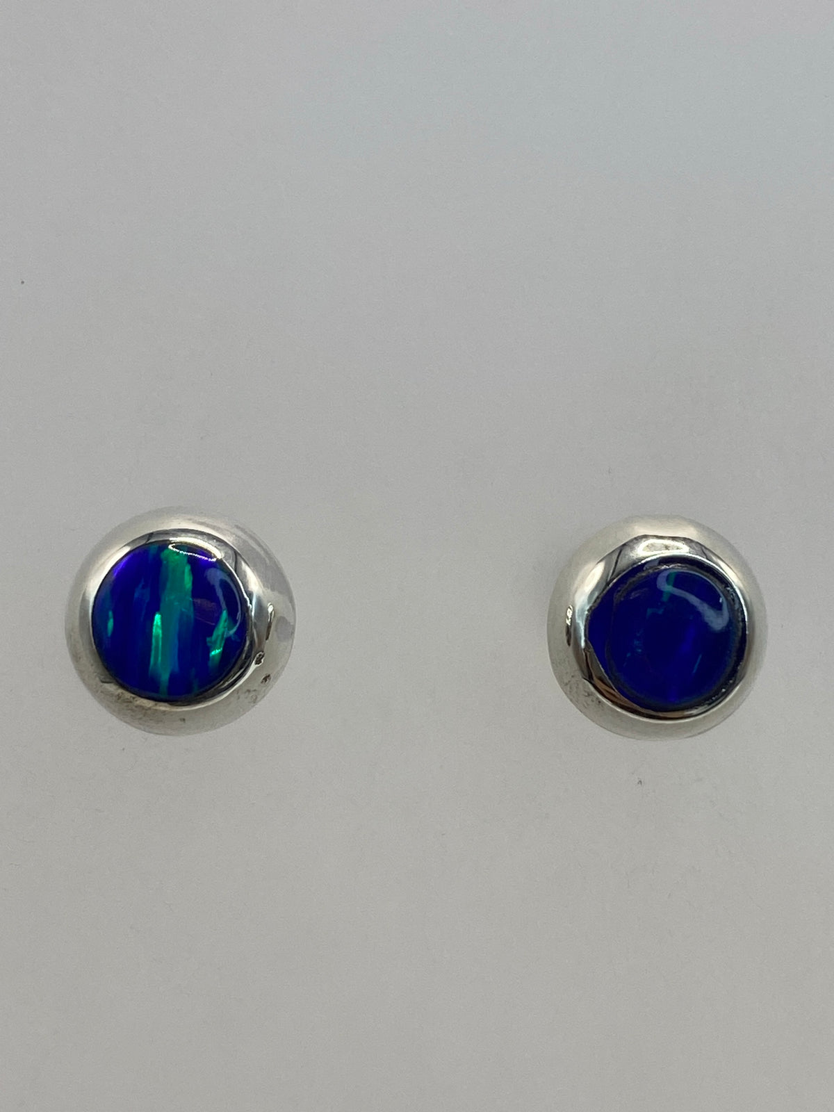 Los aretes de ópalo en la mano mostrando el tamaño compacto de 1.3 cm