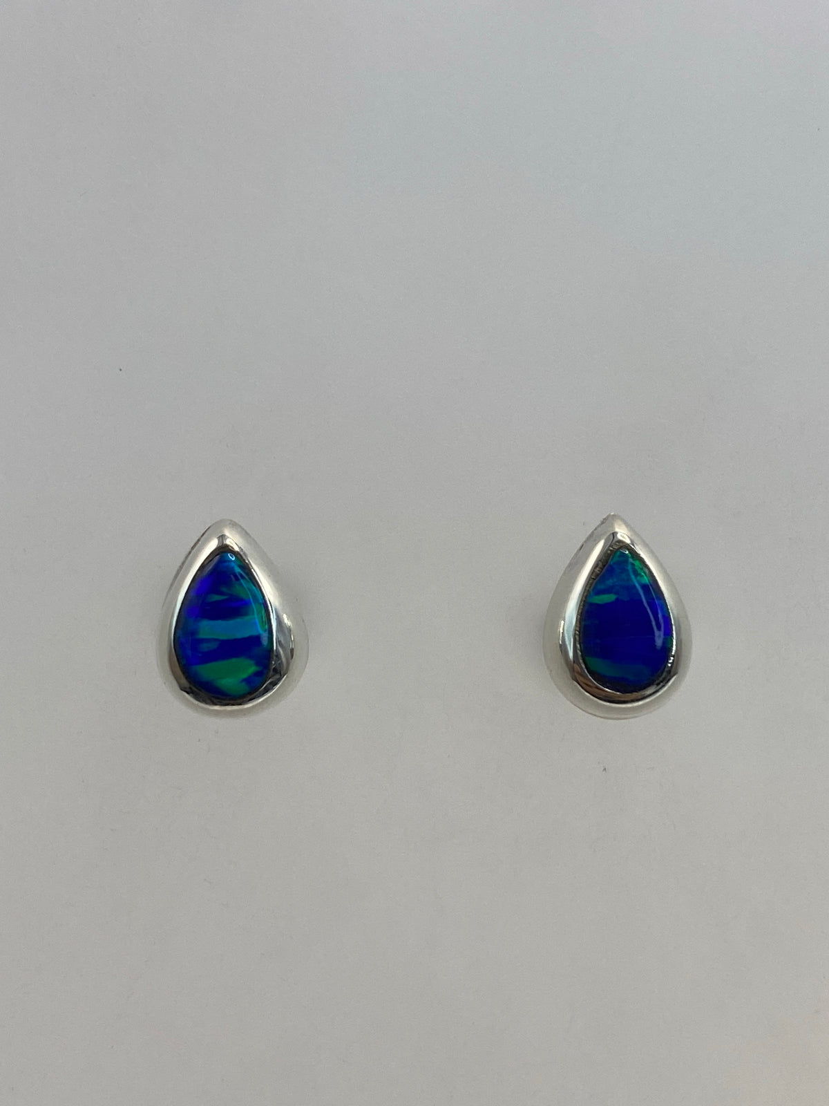 Par de aretes de plata con ópalo de fuego azul, mostrados de frente sobre fondo blanco