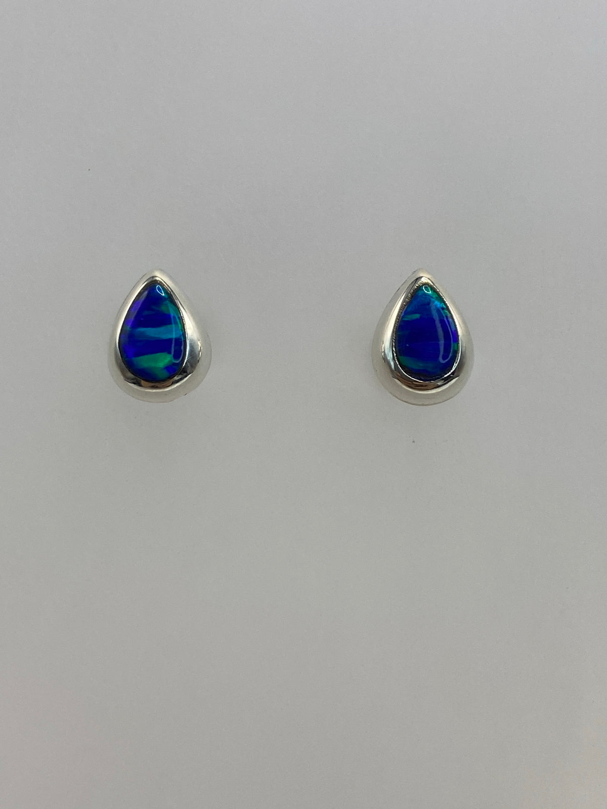 Detalle lateral de aretes de plata con ópalo azul, mostrando el engaste delicado