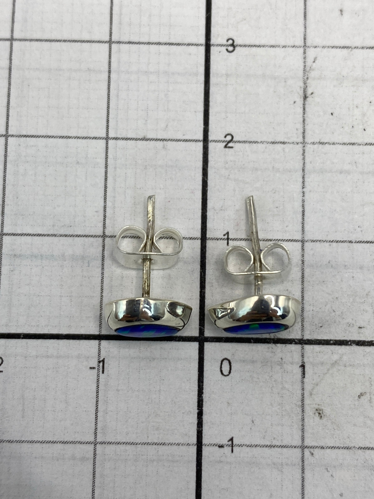 Aretes minimalistas de plata con piedra ópalo azul sobre patrón de medida