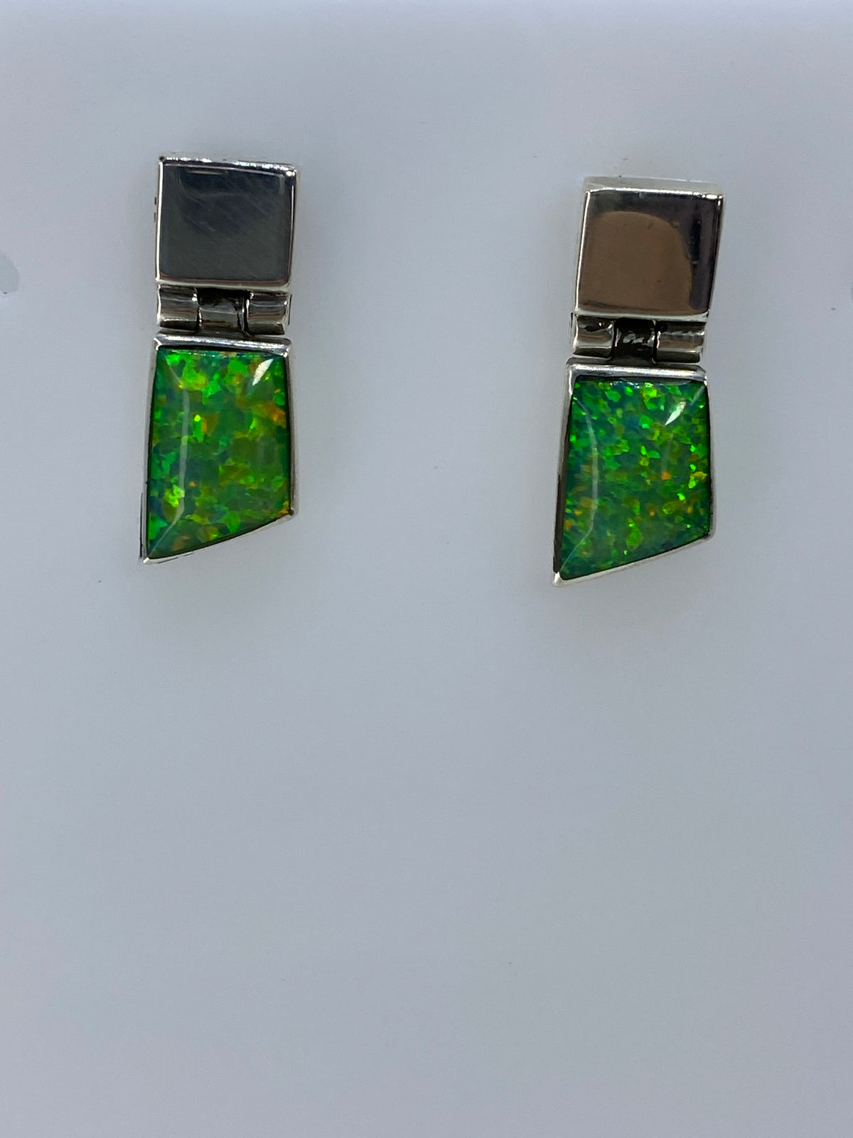 Par de aretes de plata con ópalo de fuego verde capturando luz natural, colgando contra fondo gris