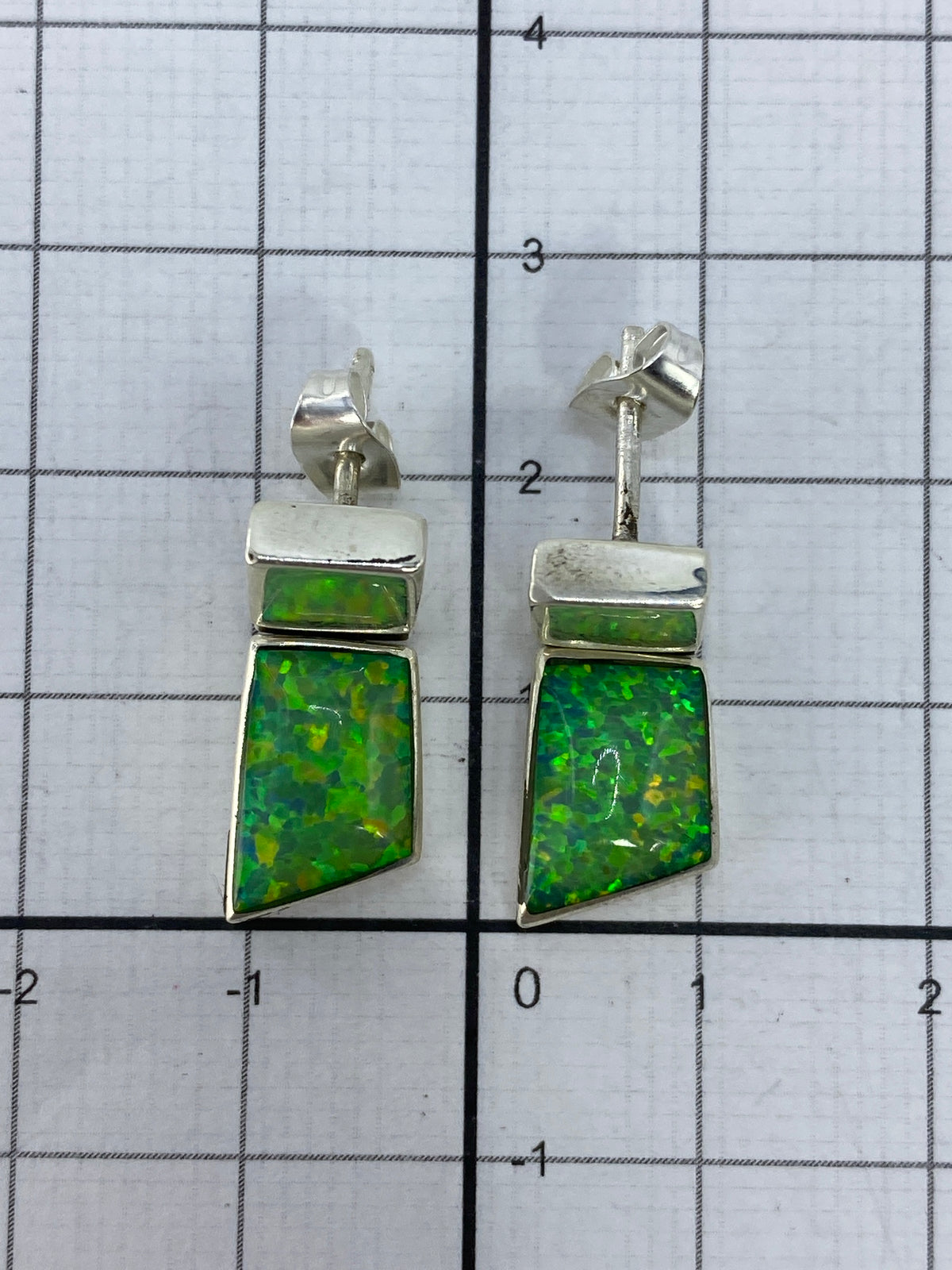 Aretes de ópalo de fuego verde colocados sobre papel cuadriculado con escala de medida
