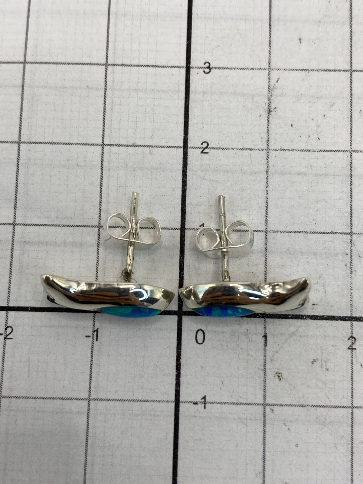 Aretes sobre escala de medición mostrando su tamaño compacto de 1.4 cm × 1.5 cm