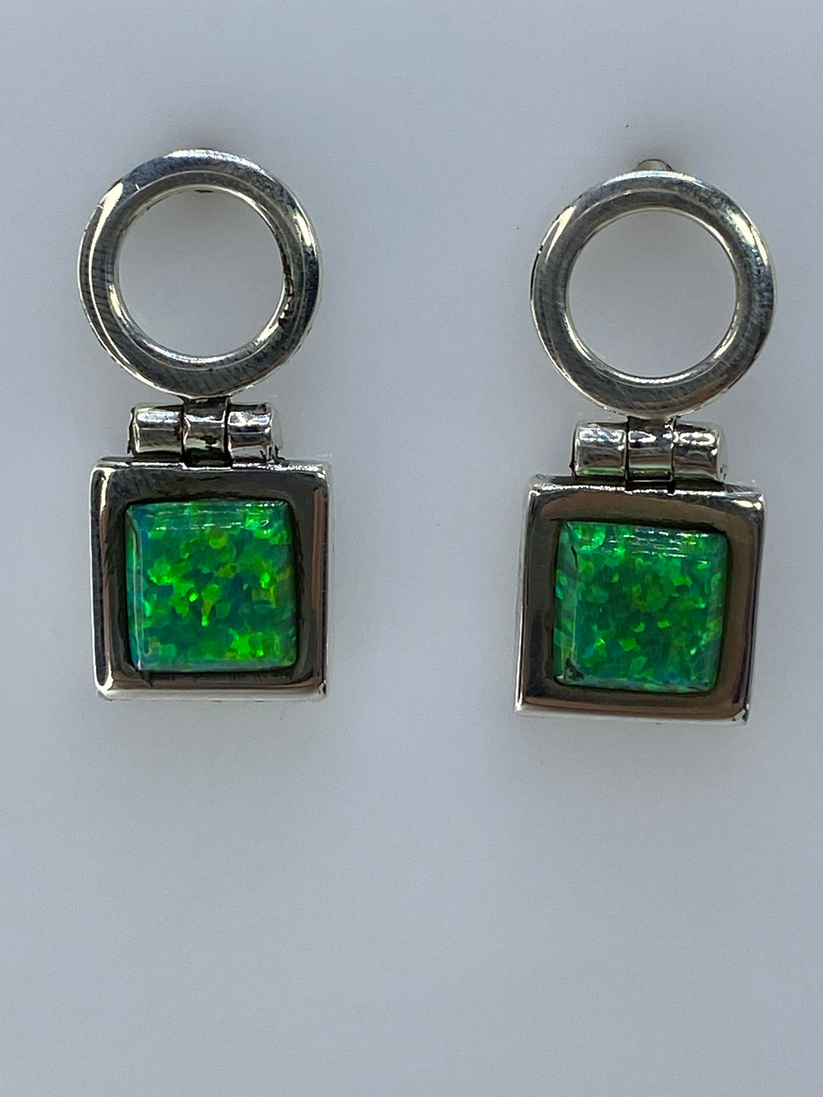 Par de aretes de plata 950 con opalo de fuego verde olivo, colgando sobre fondo blanco