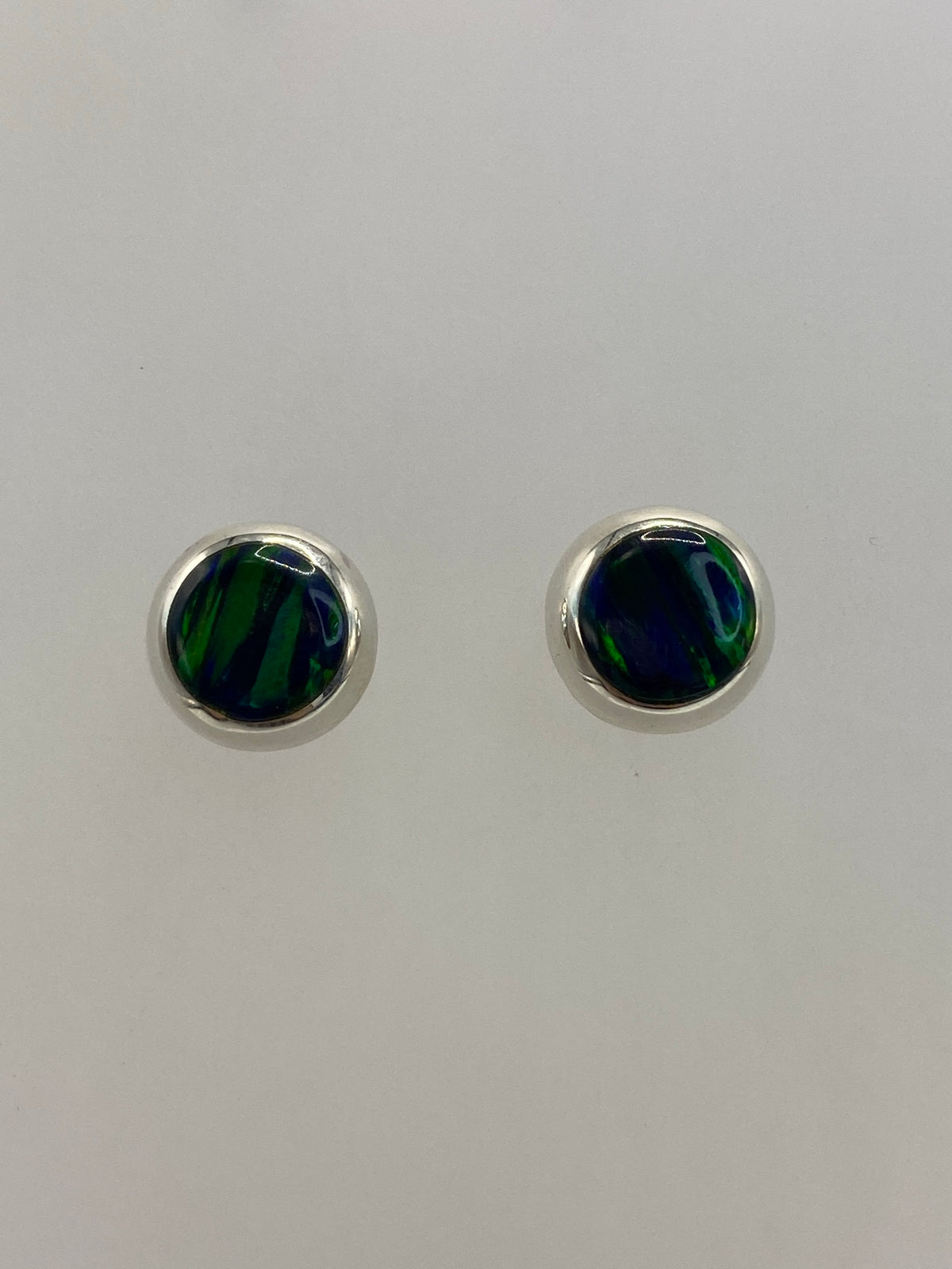 Par de aretes de plata con ópalo de fuego verde engastado, posados sobre fondo blanco