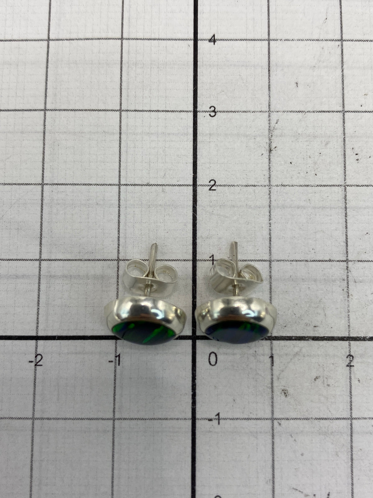 Los aretes al lado de una moneda para escala de tamaño real