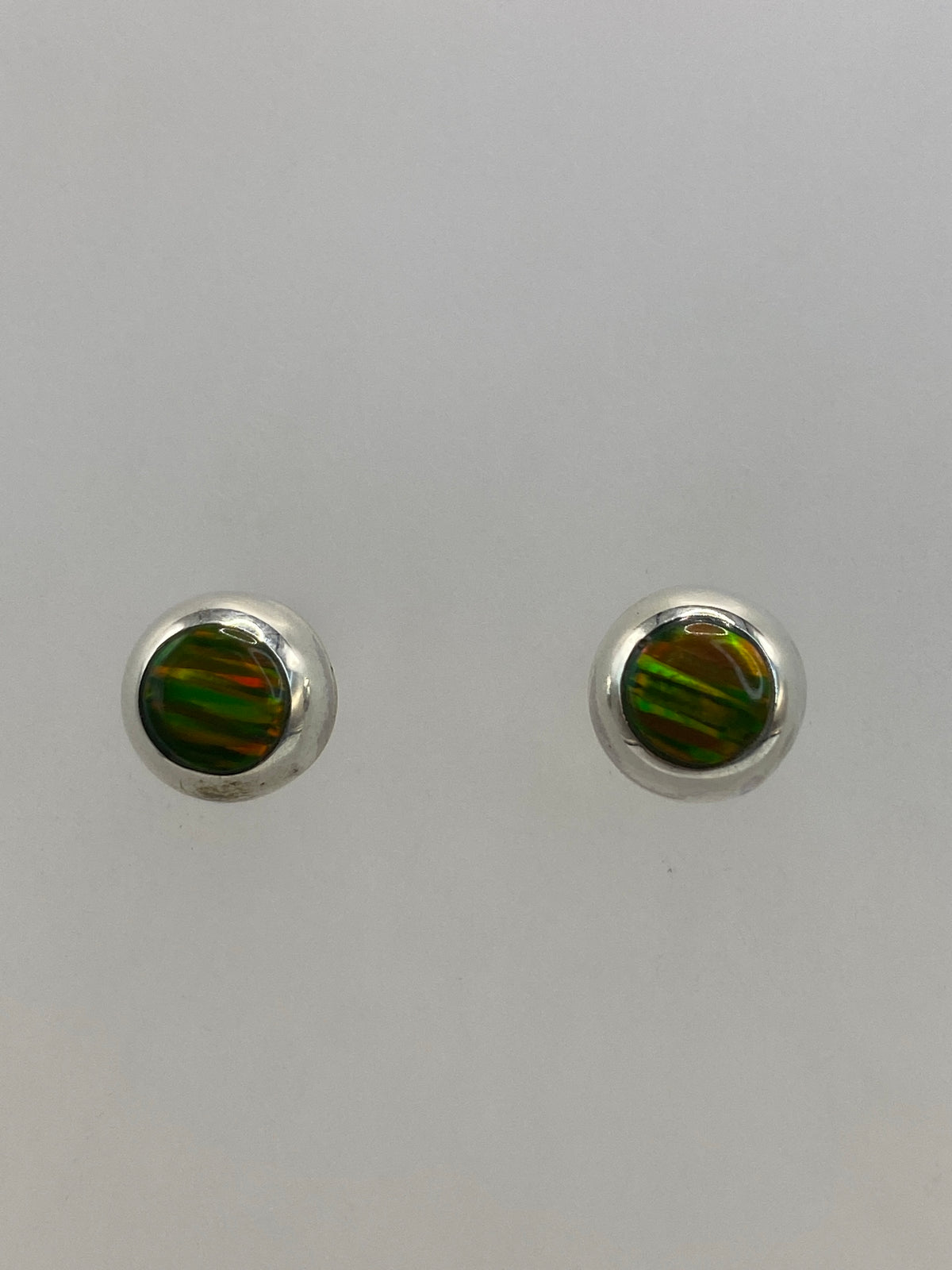 Detalle frontal de un arete de ópalo de fuego mostrando el color verde olivo y reflejos naranjas