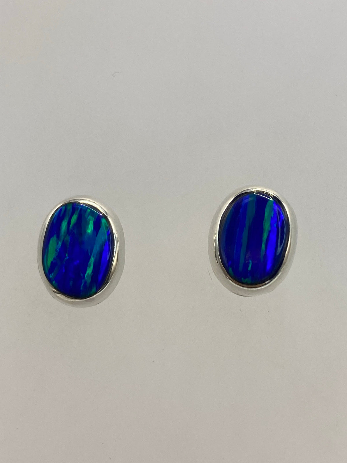 Par de aretes de plata con ópalo de fuego azul engastado, sobre fondo blanco