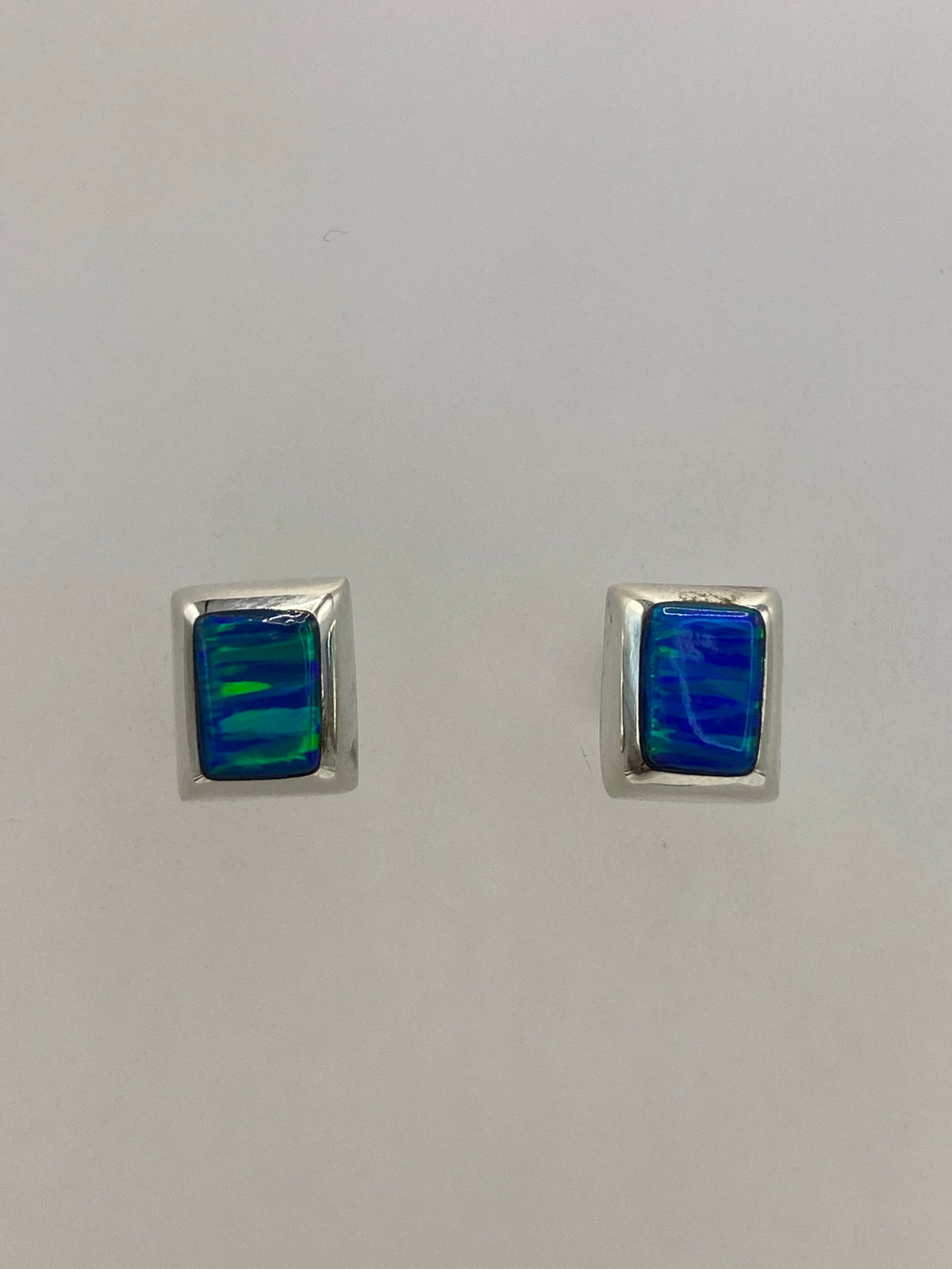 Par de aretes de plata con ópalo de fuego azul en la mano, mostrando el reflejo iridiscente
