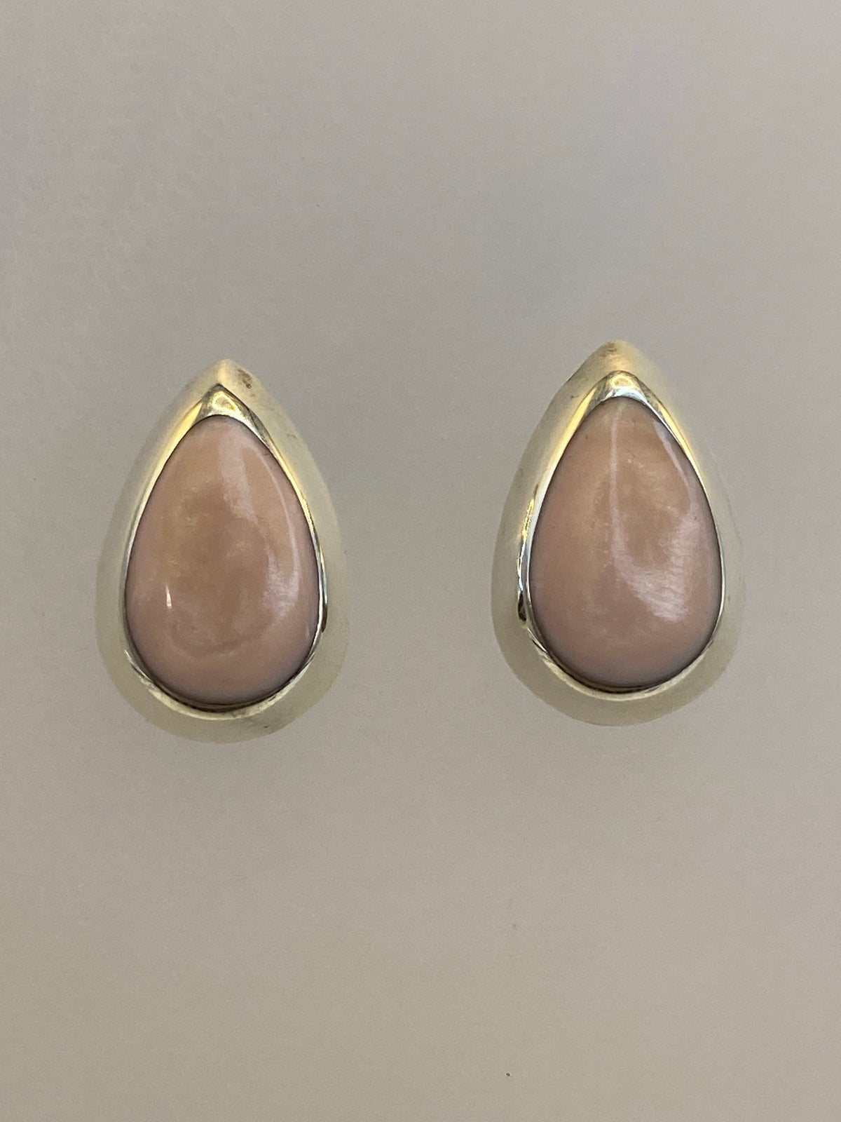 Par de aretes de plata con piedra rosa, vistos de frente sobre fondo neutro