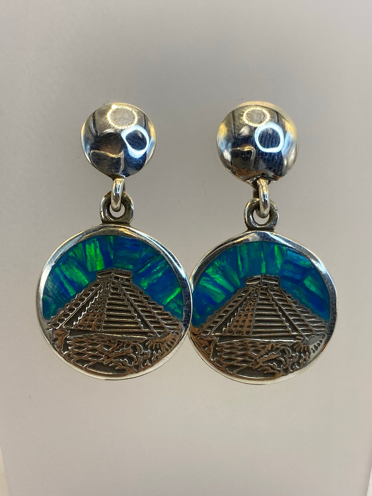 Vista frontal de los aretes mostrando el diseño prehispánico y la piedra multicolor