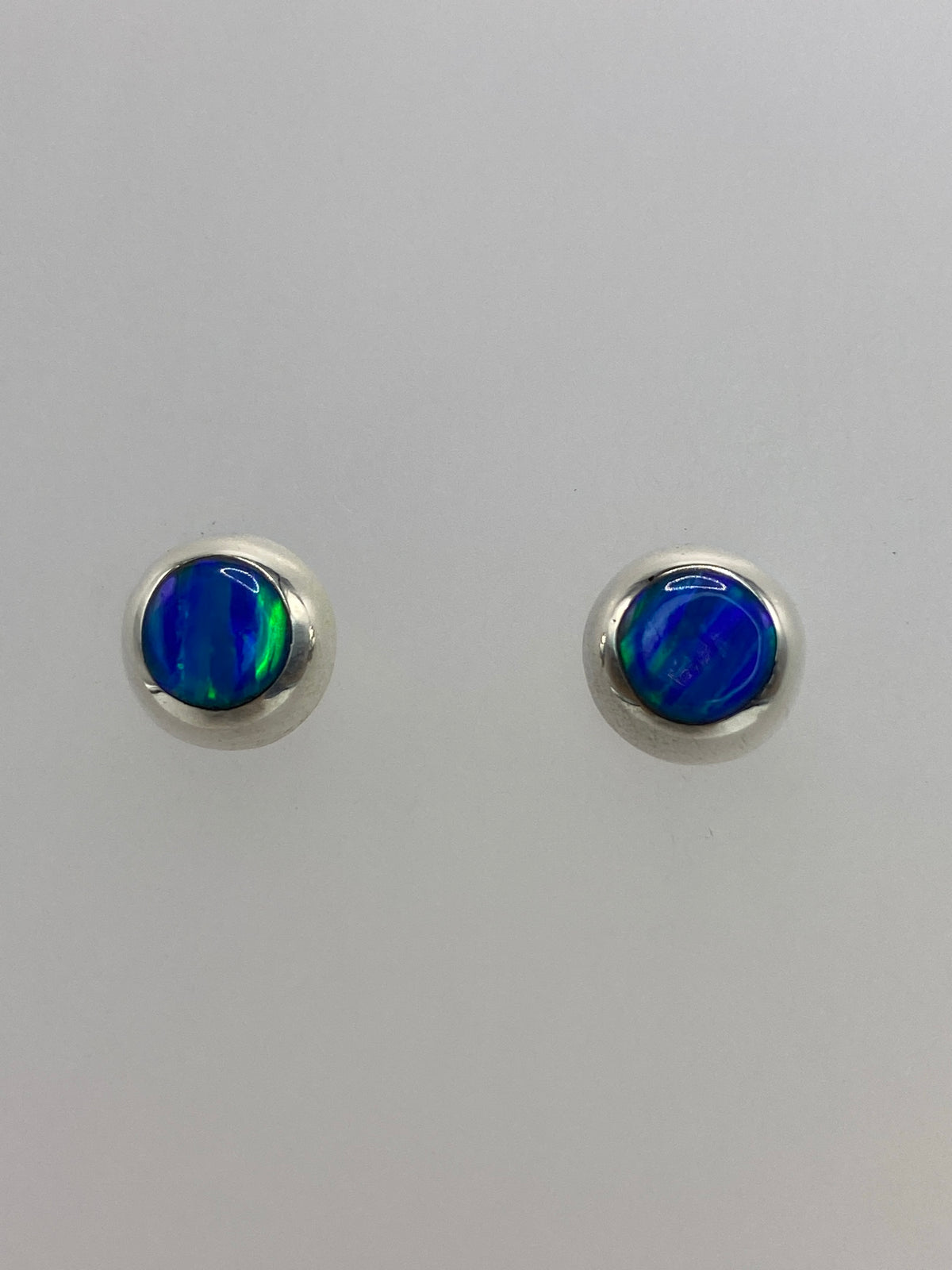 Detalle frontal de los aretes mostrando el brillo iridiscente del ópalo azul