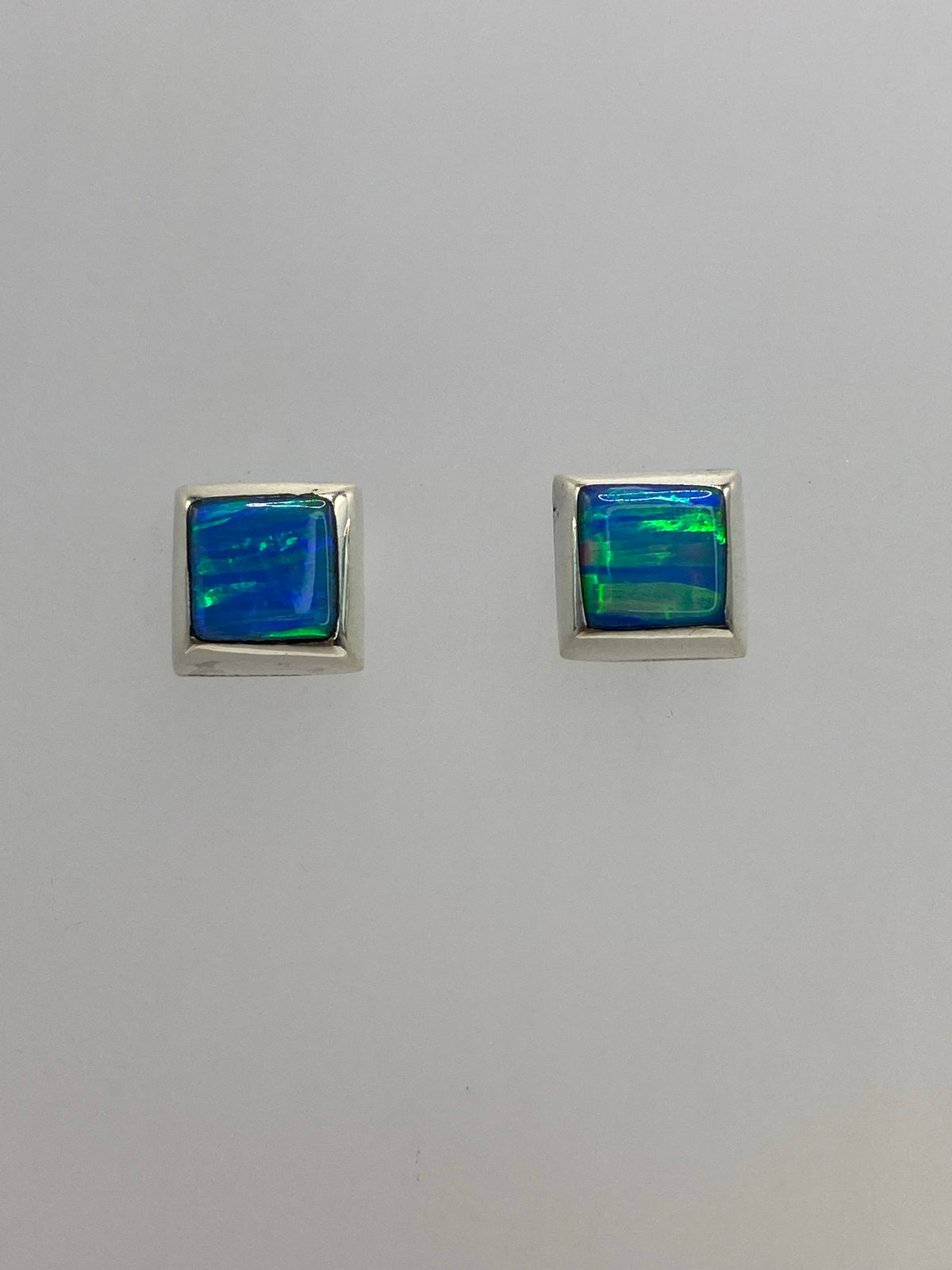 Vista frontal de los aretes mostrando el juego de luz del ópalo en ambas piedras