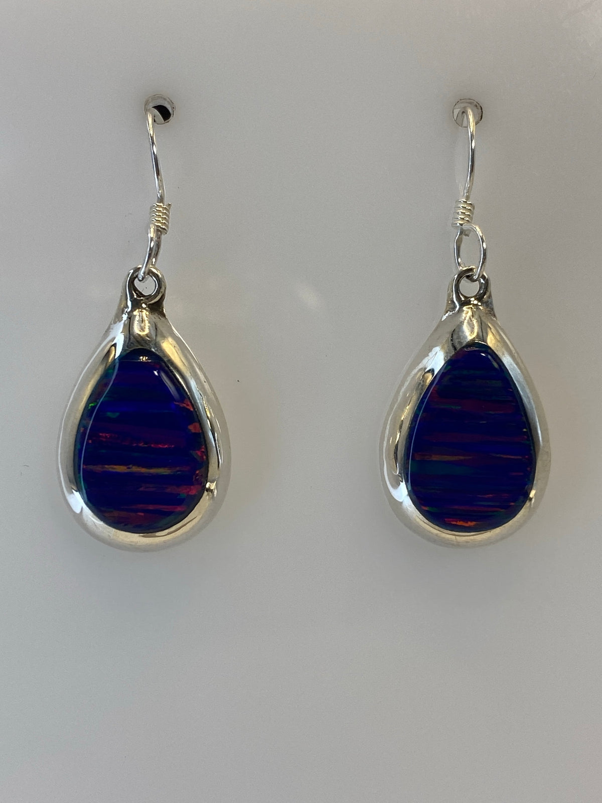 Par de aretes de plata 925 con Ópalo de Fuego multicolor colgando contra fondo blanco