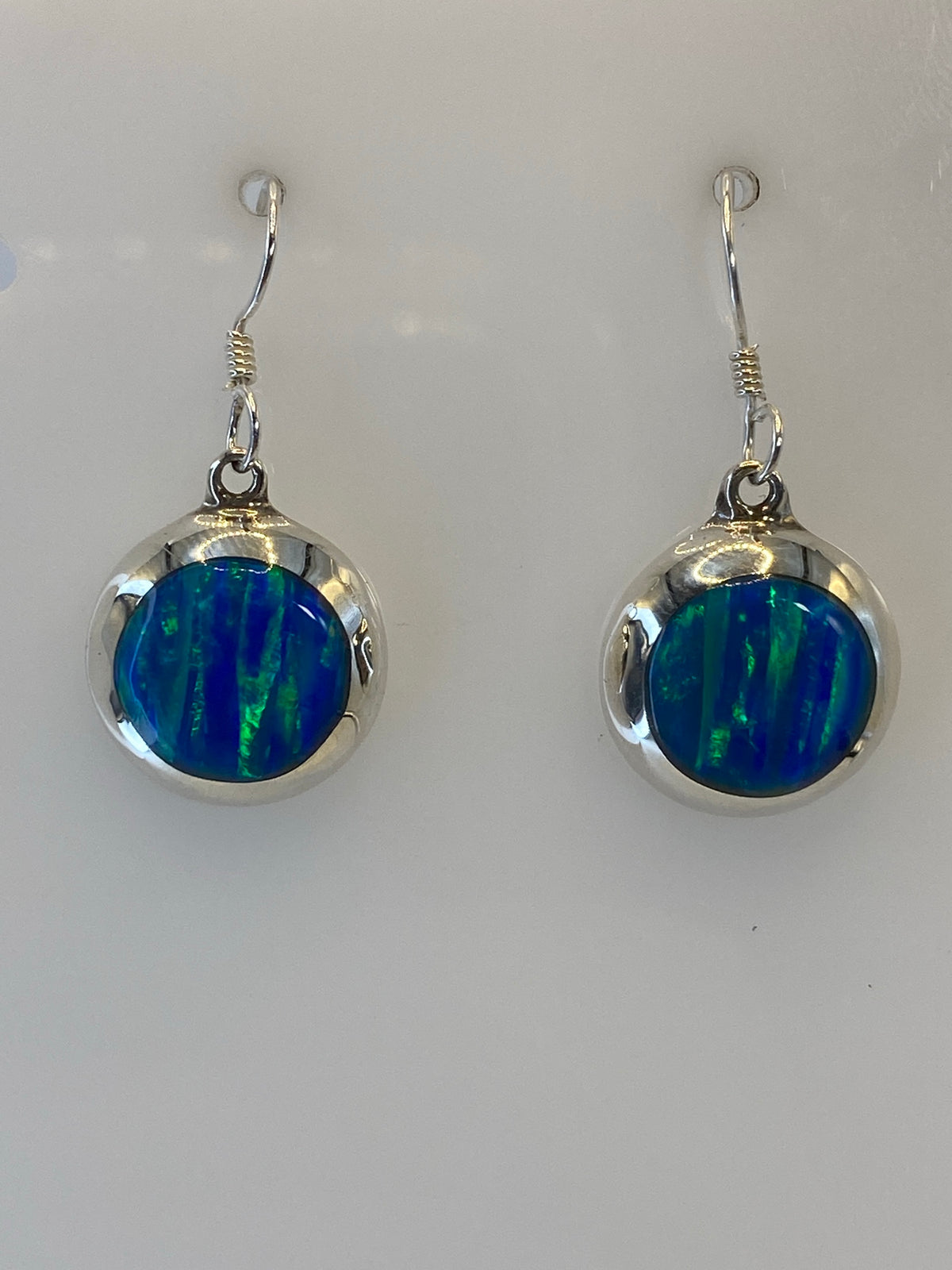 Detalle frontal de los aretes mostrando el ópalo de fuego con vetas azules, verdes y amarillas