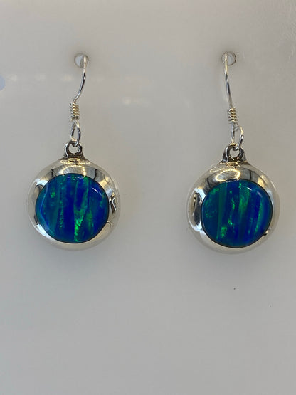 Detalle frontal de los aretes mostrando el ópalo de fuego con vetas azules, verdes y amarillas