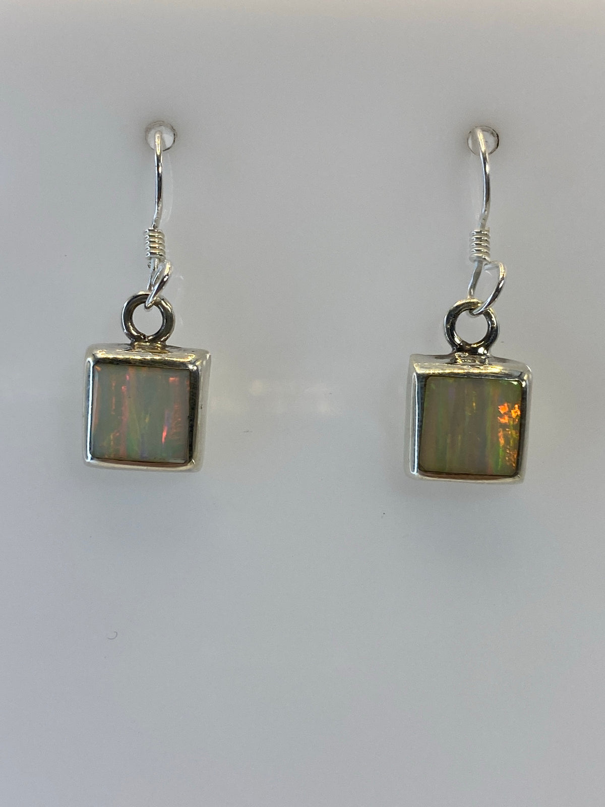 Aretes de plata con ópalo de fuego multicolor, mostrando reflejos naranjas y amarillos