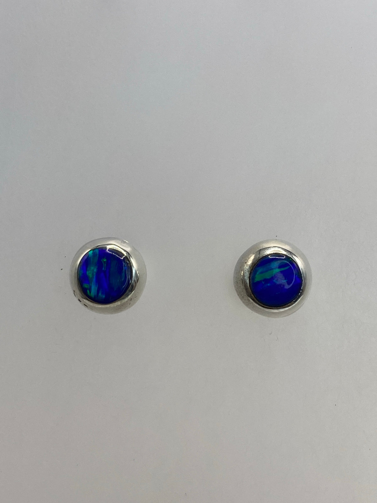 Par de aretes de plata con ópalo de fuego azul, vista frontal sobre fondo gris