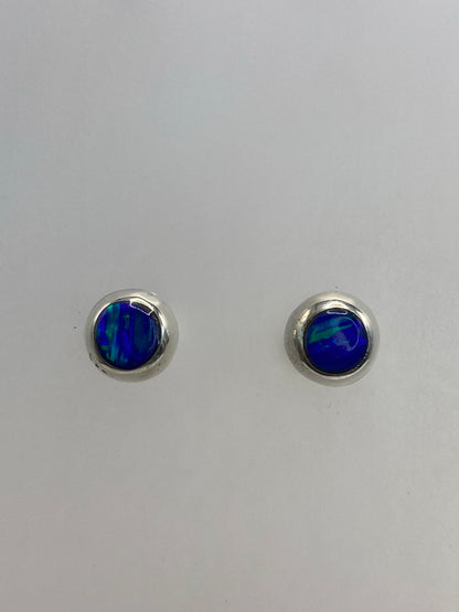 Par de aretes de plata con ópalo de fuego azul, vista frontal sobre fondo gris