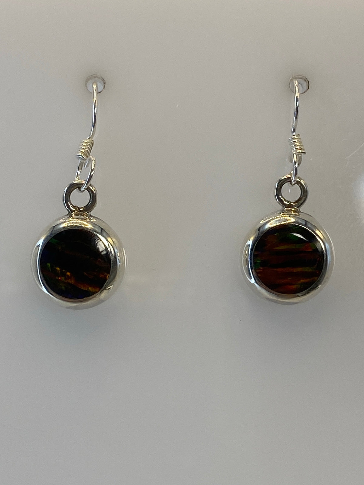 Pair of silver earrings with multicolor fire opal stones, hanging against white background