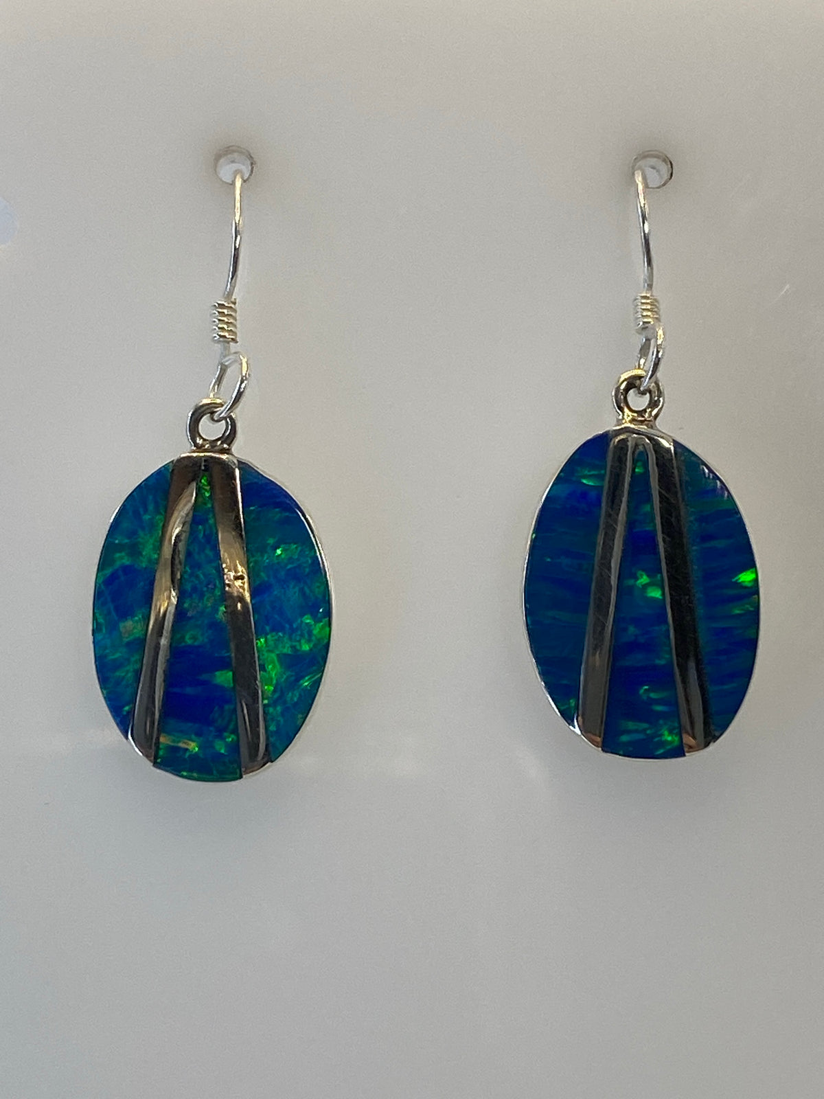 Aretes de plata con Ópalo de Fuego verde olivo colgando, mostrando los destellos de color
