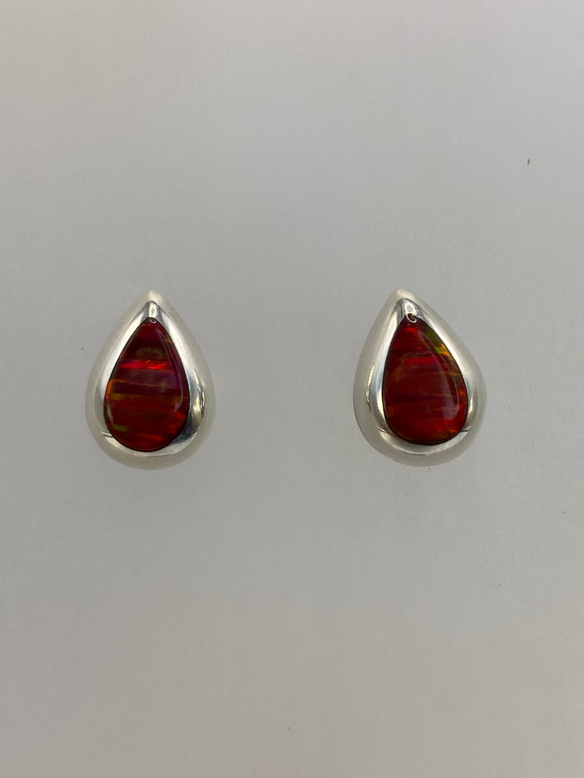 Par de aretes de plata con ópalo de fuego rojo engastado, sobre fondo blanco