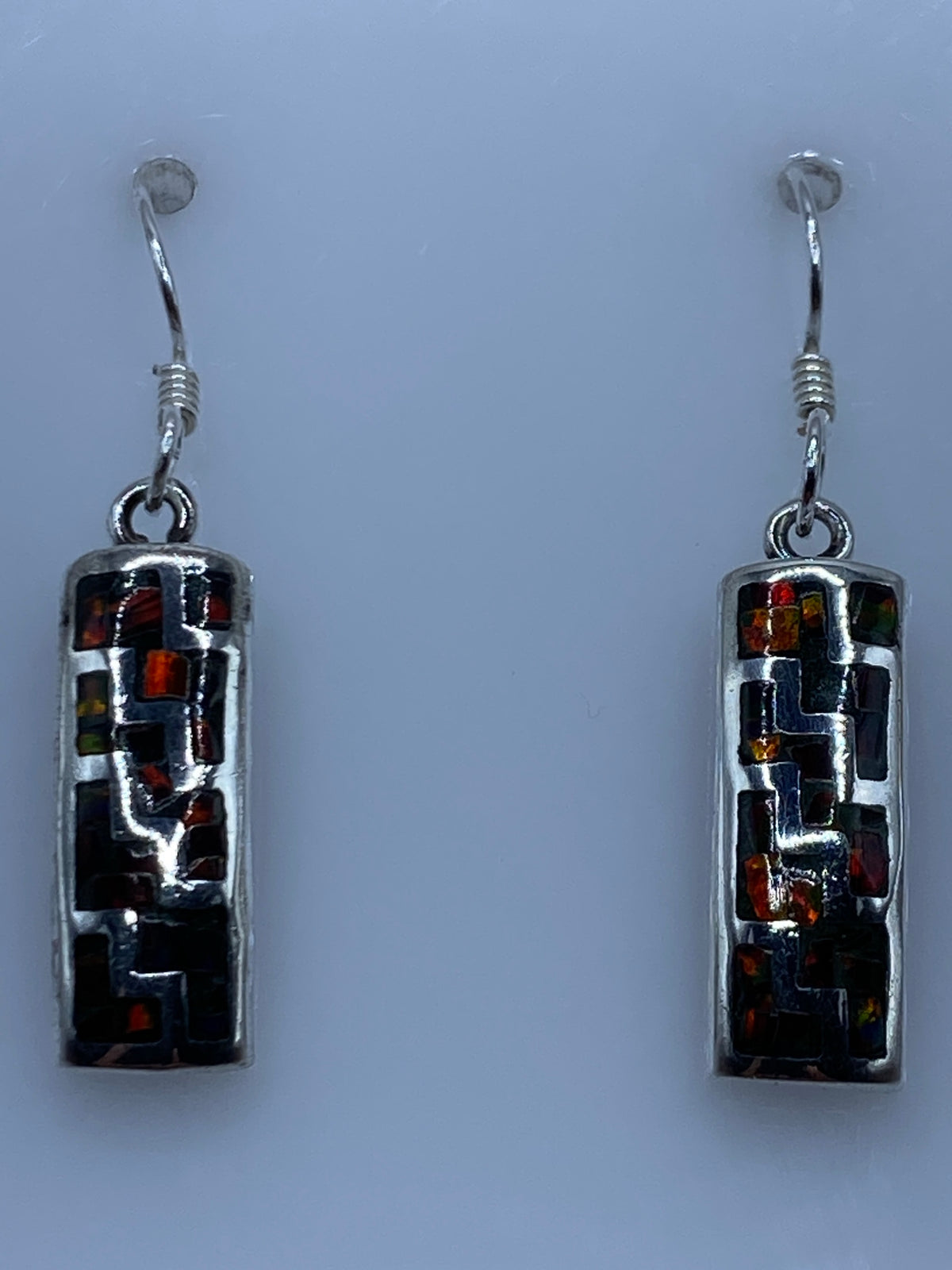 Par de aretes de plata con ópalo de fuego multicolor colgando sobre fondo gris claro