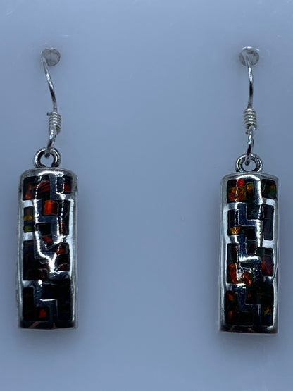 Par de aretes de plata con ópalo de fuego multicolor colgando sobre fondo gris claro