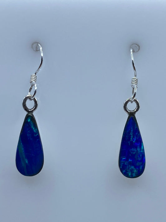 Par de aretes de plata con ópalo de fuego azul colgando sobre fondo gris