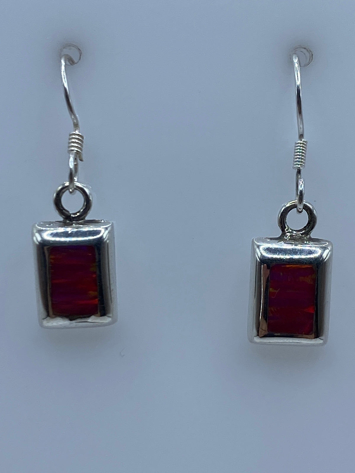 Par de aretes de plata con ópalo de fuego rosa, colgando sobre fondo gris