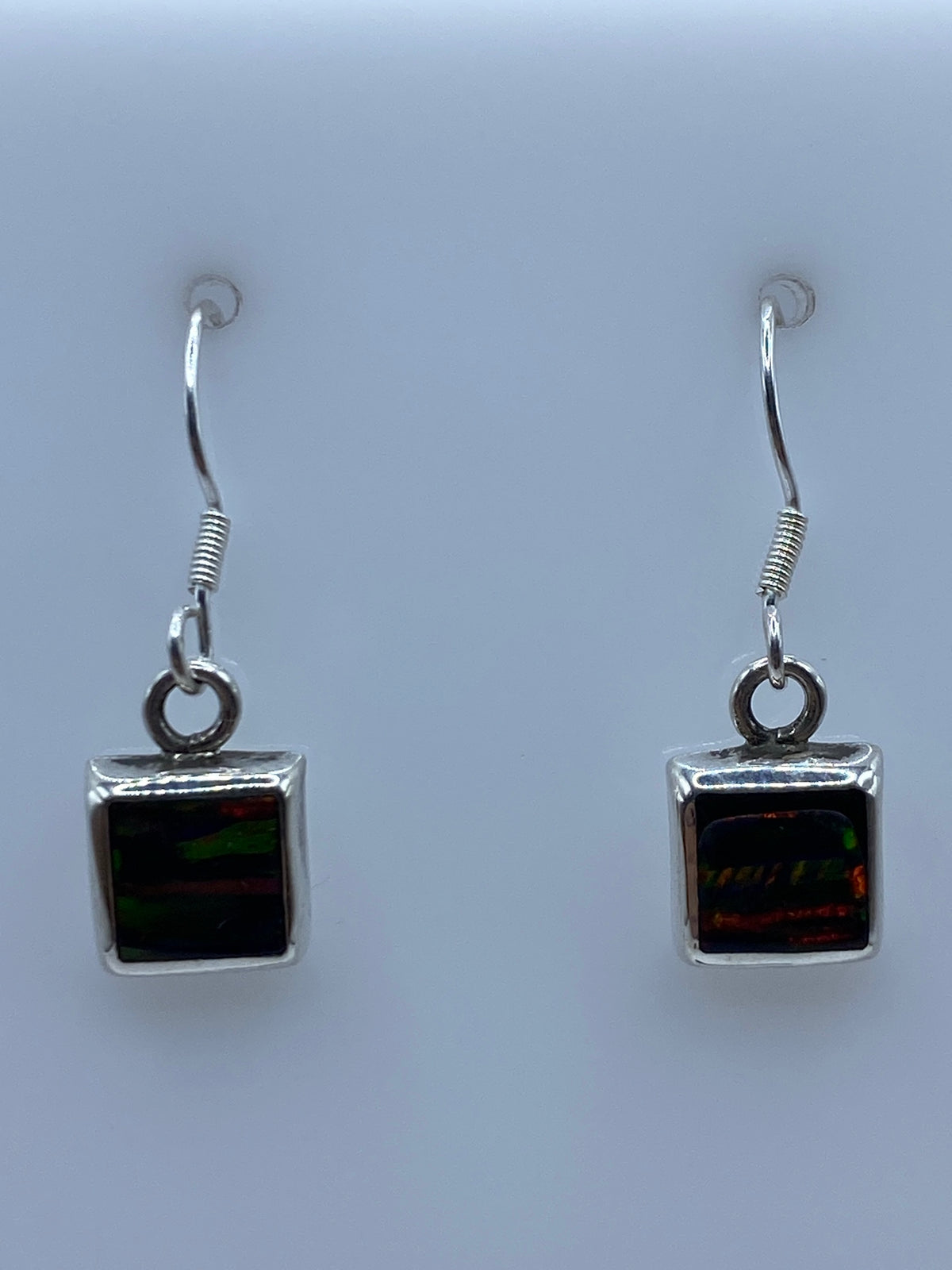 Par de aretes de plata con ópalo de fuego multicolor colgando de un ganchito de plata