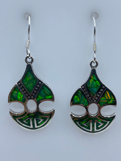 Par de aretes de plata 950 con perla verde limón, diseño prehispánico, sobre fondo blanco