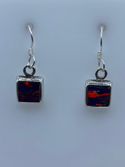 Par de aretes de plata con ópalo de fuego morada sobre fondo blanco, vistos de frente