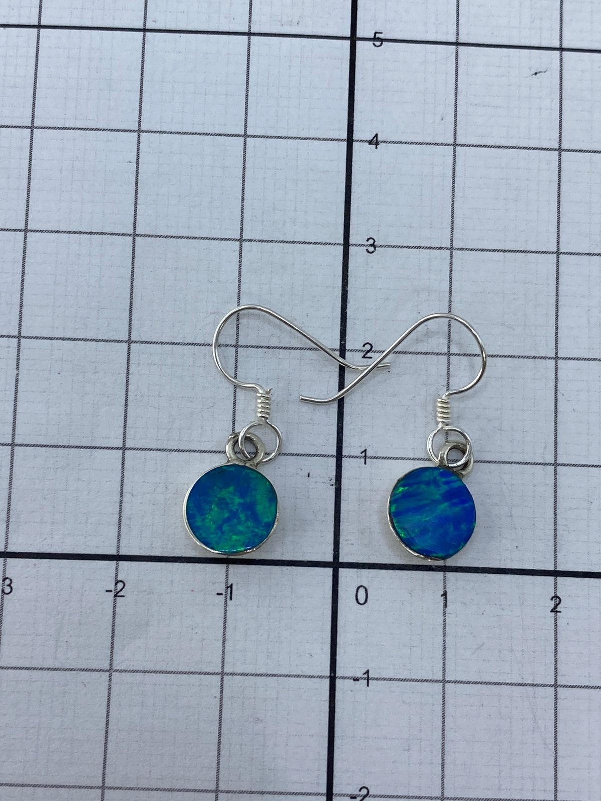 Aretes de plata con ópalo de fuego junto a regla métrica, 2.3 cm de largo