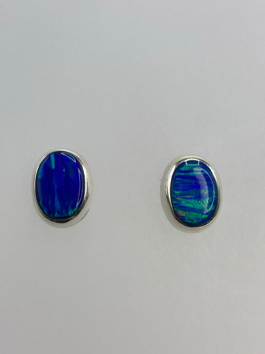 Par de aretes de plata con ópalo de fuego azul engastado, sobre fondo blanco