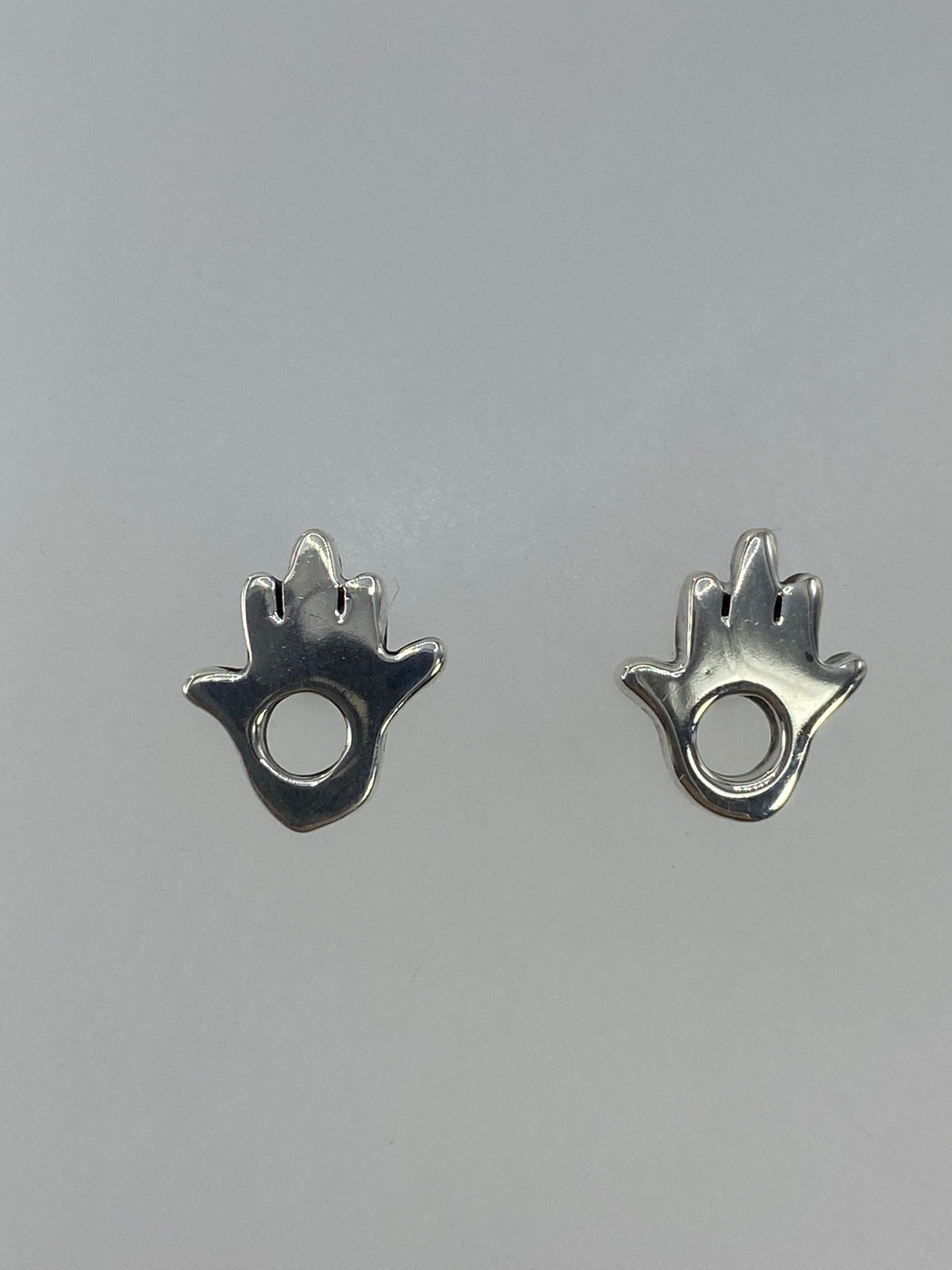 Aretes de plata cartoneado en forma de hamsa con círculo central, vista frontal