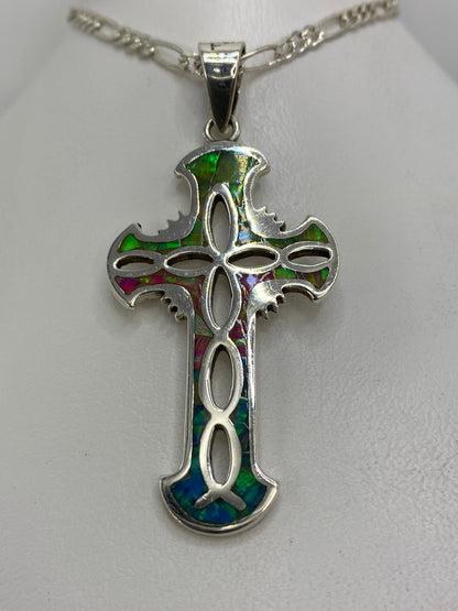Vista frontal del dije cruz religioso de plata 925 con ópalo multicolor y alas ornamentales