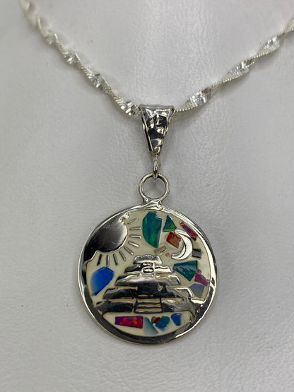 Dije de plata con ópalo de fuego multicolor y diseño prehispánico (sol, luna, pirámide) sobre fondo blanco