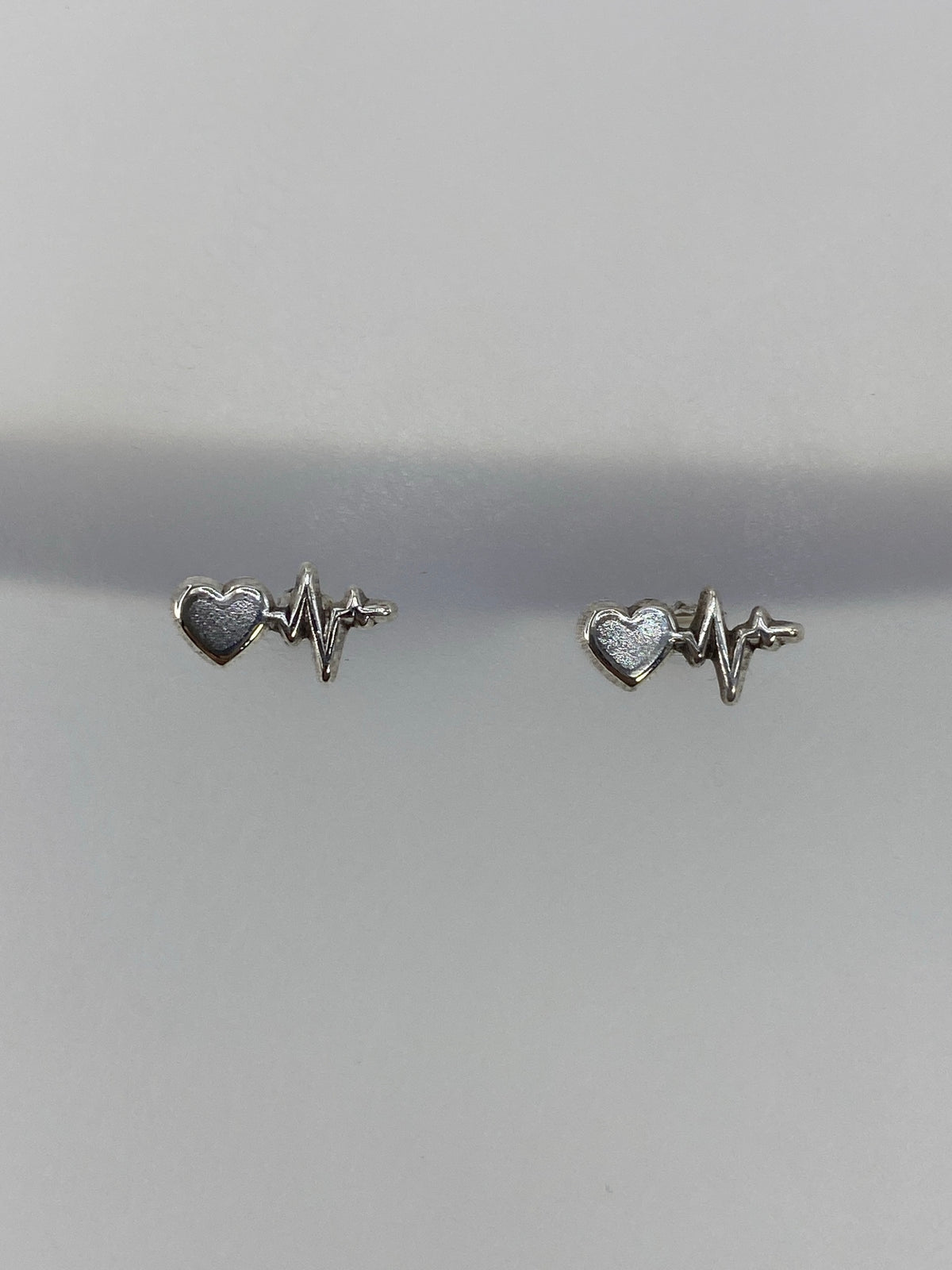 Detalle frontal de los aretes de latido: línea de ECG y corazón en plata pulida