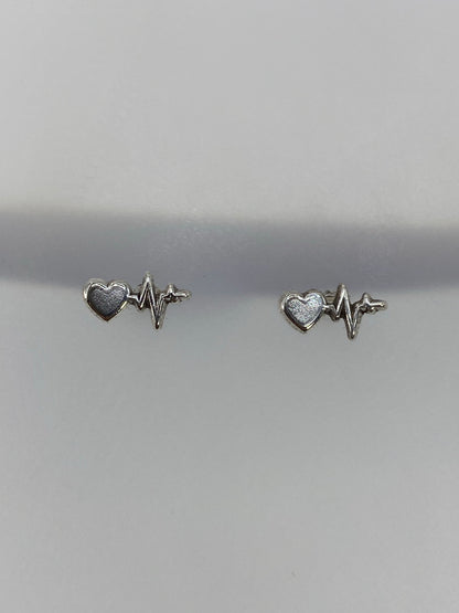 Detalle frontal de los aretes de latido: línea de ECG y corazón en plata pulida