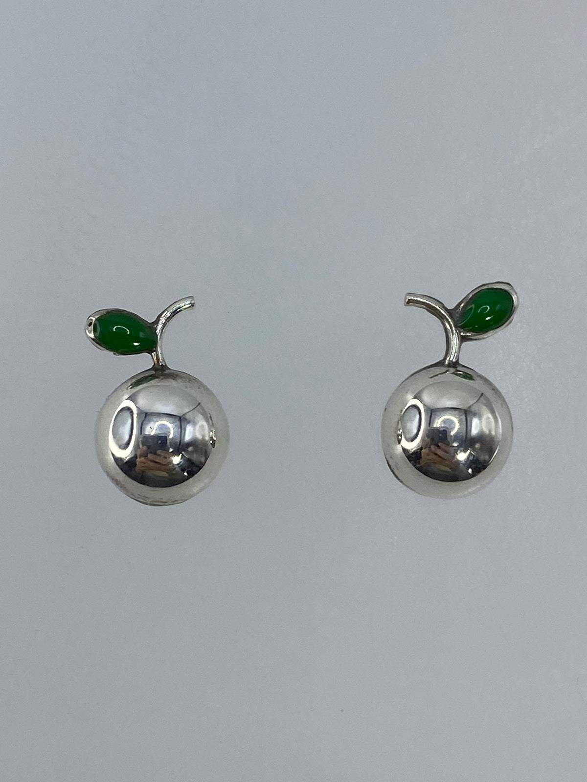 Aretes pequeños de plata cartoneado del tamaño de una perla sobre fondo blanco