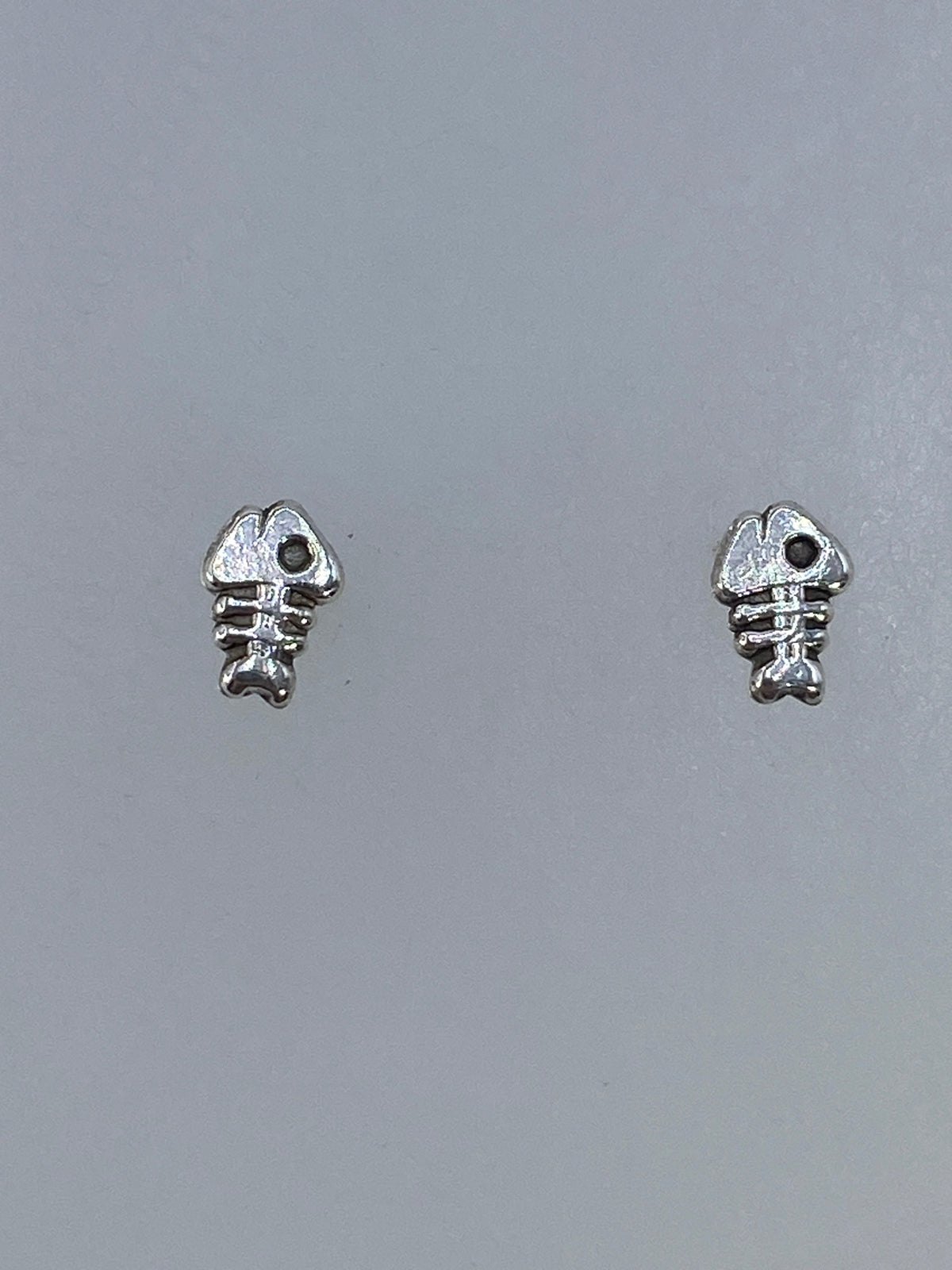 Aretes de plata cartoneado en forma de espina de pez, minimalistas y elegantes, posados en plano