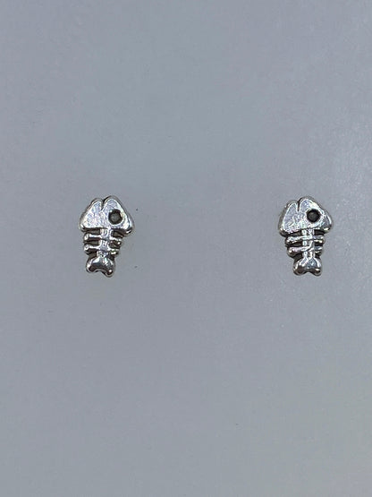Aretes de plata cartoneado en forma de espina de pez, minimalistas y elegantes, posados en plano