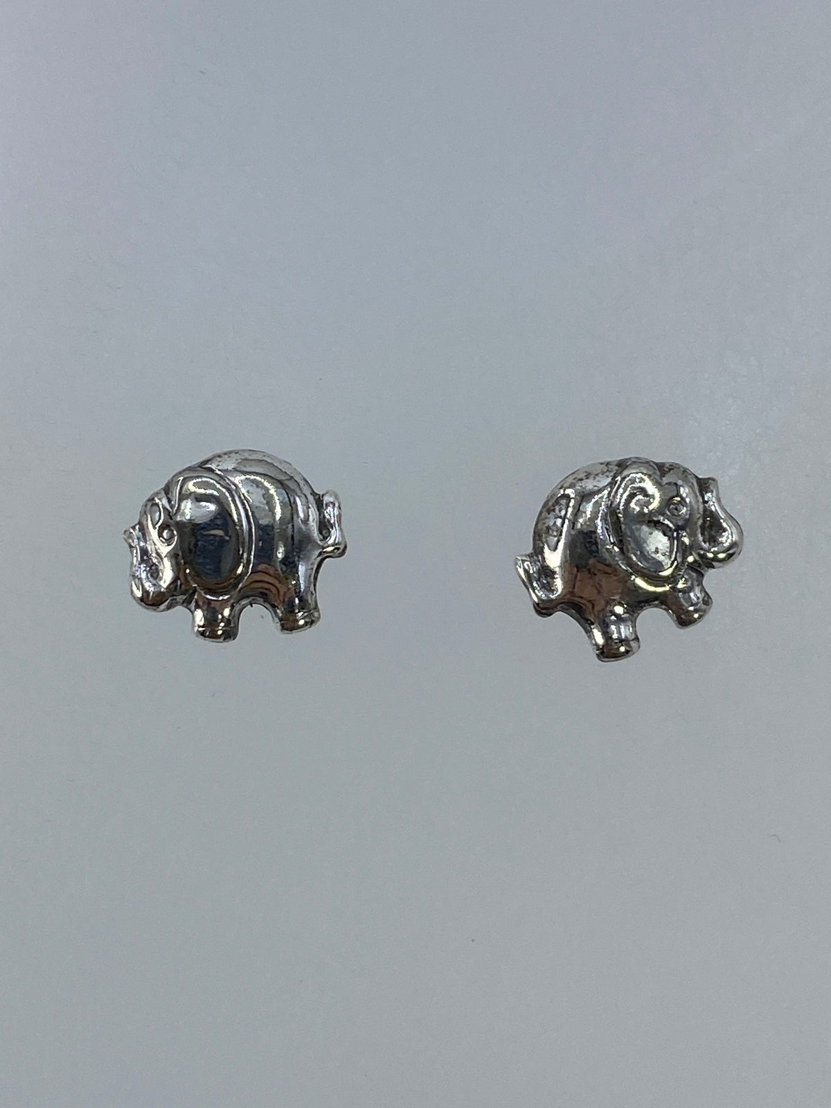 Aretes de plata elefante en cartoneado, vistos de frente sobre fondo gris