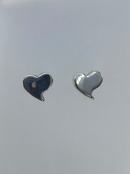 Vista frontal de los aretes corazón de plata pulida reflejando la luz