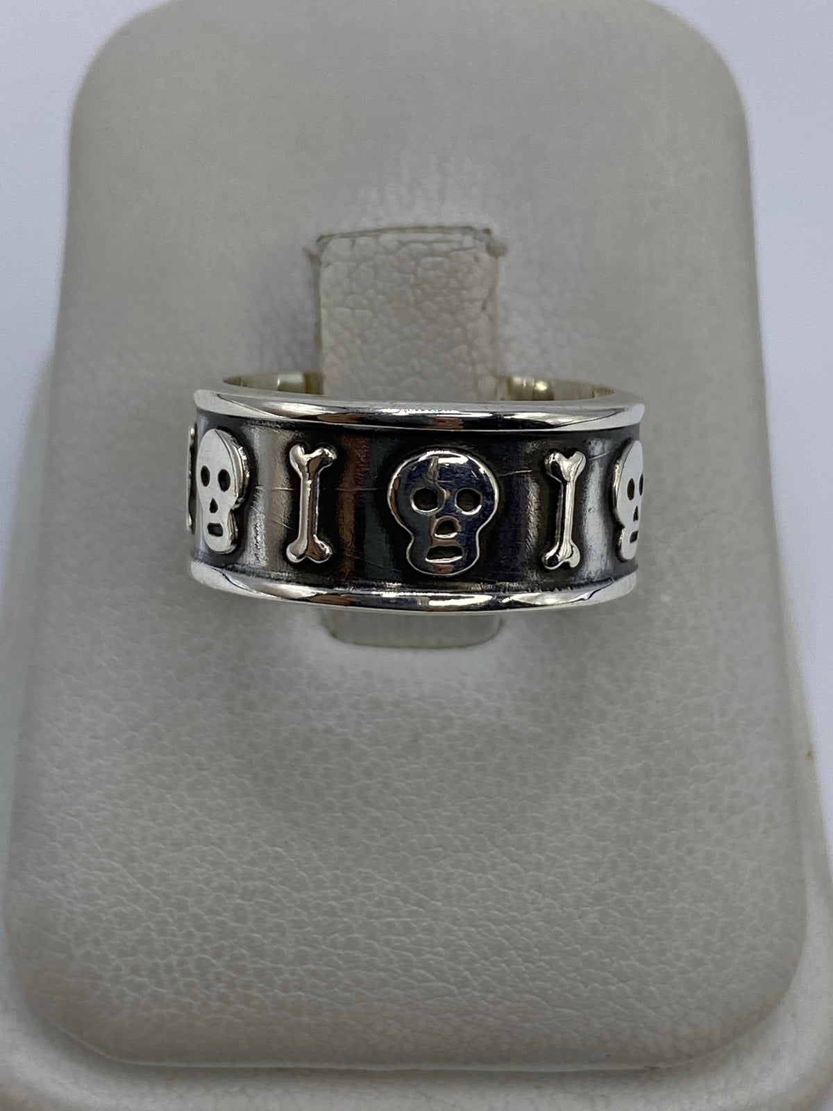 Anillo de plata repujado con calavera y huesos alternados en relieve, sobre fondo blanco