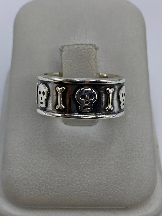 Anillo de plata repujado con calavera y huesos alternados en relieve, sobre fondo blanco