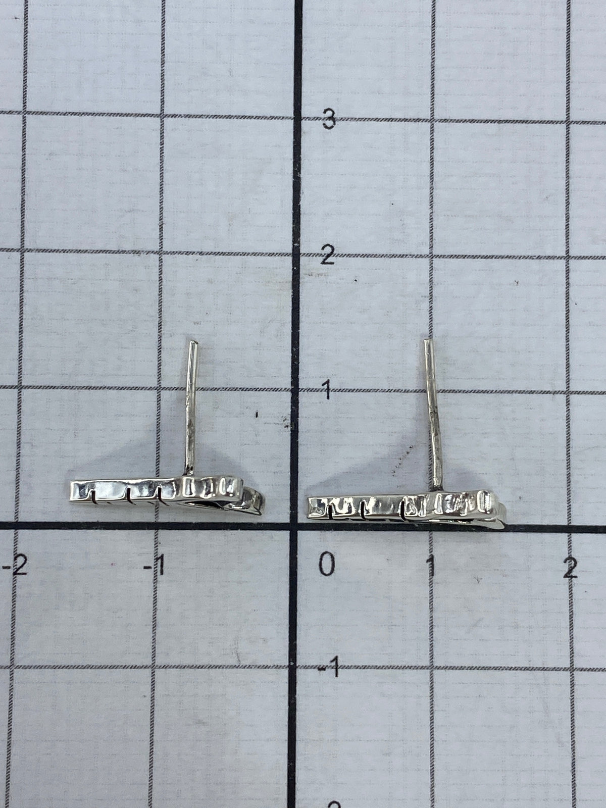 Los dos aretes juntos con escala de centímetros, mostrando su tamaño pequeño de 1.3 cm