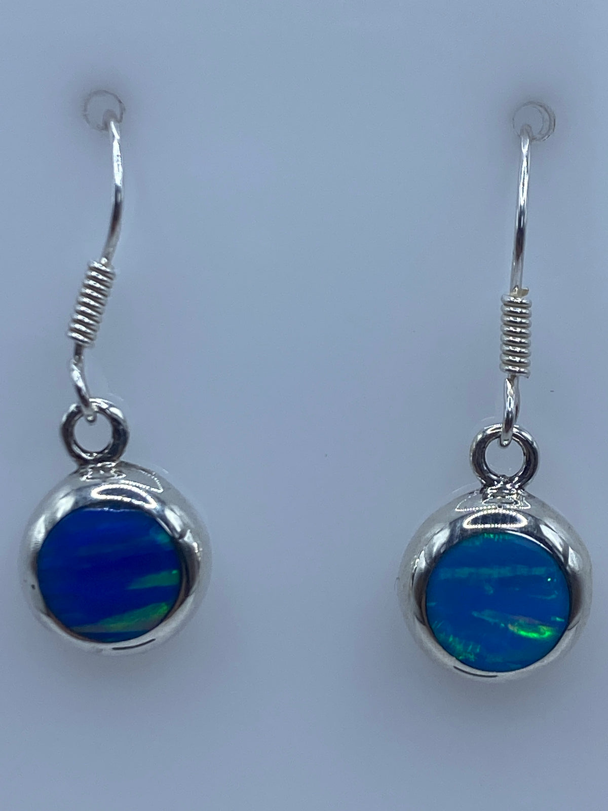 Aretes en la palma de la mano mostrando el tamaño delicado y el tono azul del Ópalo