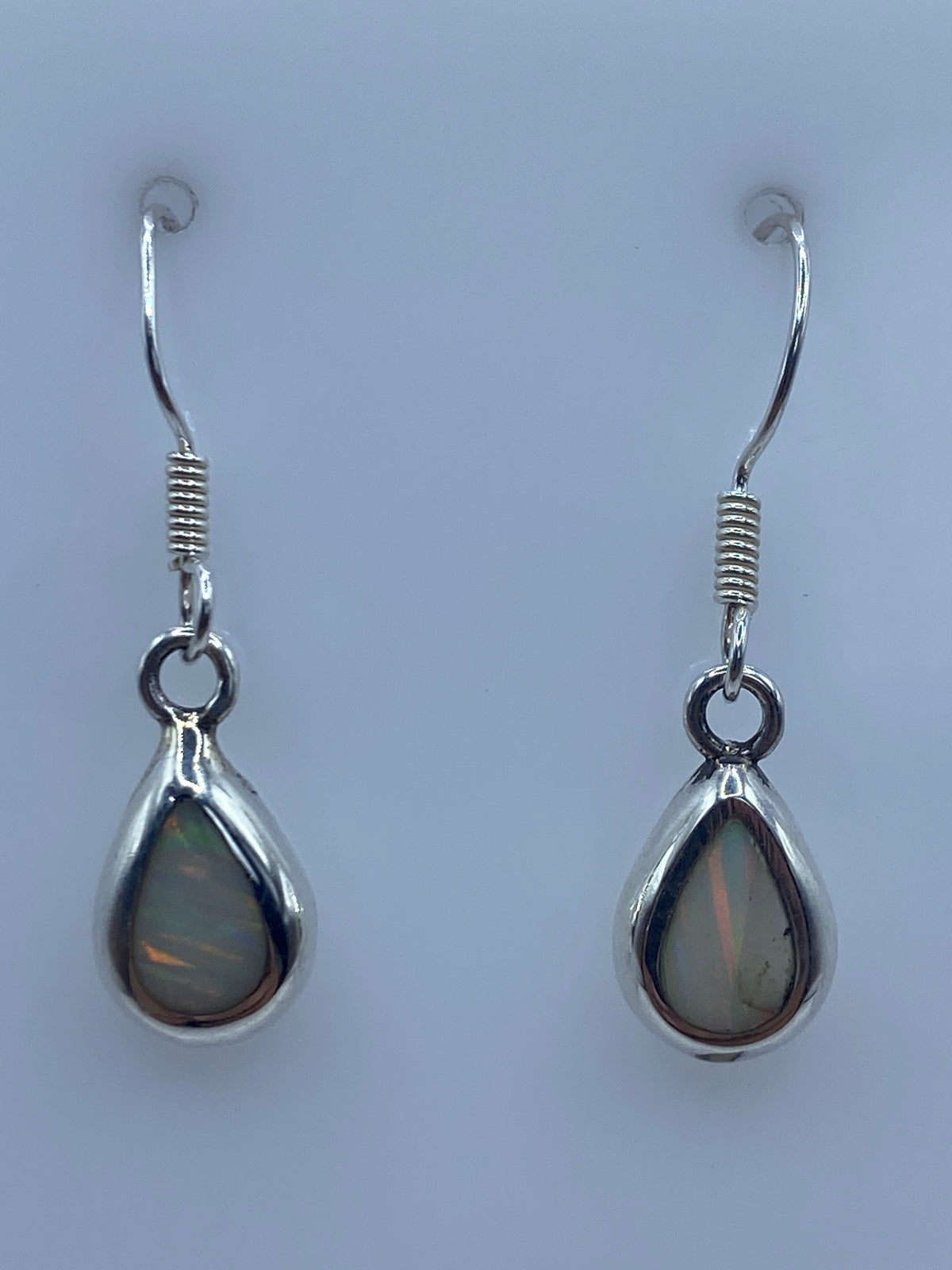 Aretes de plata 950 con Opalo de Fuego en forma de gota, mostrando tonos naranja y dorado bajo luz natural